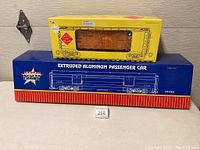 Two boxed model train cars: blue box labeled Extruded Aluminum Passenger Car by USA Trains and yellow box labeled Aristo Craft Trains Steel Reefer Car