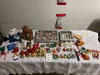 Full overview of assorted ornaments laid out on a white cloth, showing variety of colors and types including baubles, figurines, and novelty shapes