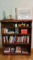 Wooden shelving unit displaying various items including books, wooden toy truck, framed fighter plane drawing, copper candlesticks, candles, and the practice chanter standing upright.