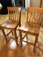 Pair of wooden bar stools with slatted backs and flat seats, placed on hardwood floor