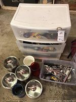 Top view showing plastic storage drawers filled with fishing reels and miscellaneous items. Several metal canisters with lids placed beside a clear plastic container holding silverware and other small objects.