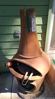 Full front view of terracotta chiminea showing firebox opening, grill grate and metal tools inside