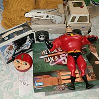 Overview of lunchbox, Mr. Incredible figurine, toy round face, board game box and toy tow truck