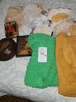 Crocheted doilies and tablecloths in various colors, featuring a bright green crocheted piece and yellow and cream items alongside baskets and a tin box.