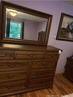 Front view of wooden dresser with attached mirror showing drawers, decorative trim, and metal handles.