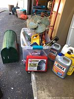 Full lot overview showing tire chains in red case, vintage GE metal fan, green mailbox, various car oil containers, and part of a long black rubber container underneath.
