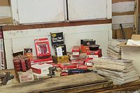 Wide view of laid out Grote and DIETZ automotive parts, including boxed rear lamp modules, reflectors, and various mechanical parts on a wooden surface with stacked QST Magazines at the side.