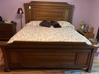 Full frontal view of king size wooden bed frame with floral bedspread and pillows. Shows footboard and headboard design.
