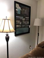 Lamp with dark turned base and cream fabric shade illuminated near a couch and wall outlet