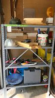 Full view of metal shelving unit with workshop items including wood, tools, buckets, and hardware
