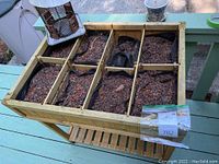 Front-top view of wooden raised planter showing divided sections filled with soil and lined with black fabric, some pots placed on planter.