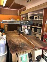 Wide view of Wards Powr-Kraft radial arm saw on a wooden table with shelves and miscellaneous items in background.