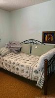 Twin size metal frame daybed with mattress, sheets, and pillows in a room with light colored walls and brown carpet.