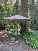 Wide view of large beige sunshade umbrella in wooded outdoor setting showing umbrella and base made with cinder blocks