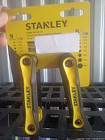 Photo of Stanley folding hex key set in original packaging. Shows yellow handles with black Stanley branding, the folding mechanism, and partly visible size details on the package.