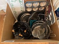 Photo of a cardboard box filled with various bakeware items including Bundt pans, muffin pan, cookie cutters, strainers and baking trays.