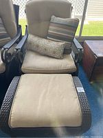 Outdoor chair with beige cushions and two matching decorative pillows, dark brown plastic rattan weave metal frame on blue carpet