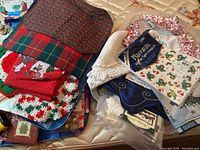 Overview of assorted Christmas linens including red and green plaid fabrics, red cloth with holiday embroidery, and white crocheted edges