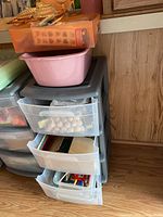Photo of pink and gray plastic storage container with four drawers containing assorted craft supplies including beads and papers.