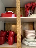 Corelle dinnerware including stacked plates, bowls in white with red rims, and red mugs, along with red serving utensils.