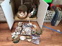 View of basket filled with assorted sea shells including large conchs and sand dollars, the shell wreath, Florida shaped serving tray, and loose shells in plastic bags on the floor.