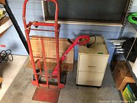 Photo showing three main items: red hand truck, metal two-drawer filing cabinet in cream color, and red electric edger.