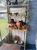 Full view of the metal and wood bakers rack with items displayed on shelves (not included in sale). Rack has metal sides with circular decorative pattern and wooden shelves.