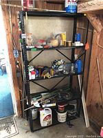 Metal shelving unit filled with assorted hardware, tools, and paint supplies located in a wood-paneled room.