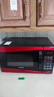 Entire microwave showing red and black exterior, placed on countertop beneath wooden cabinets.