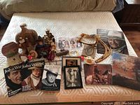 Lot contents including pottery pieces, John Wayne books and magazines, Western figurines, decorative headdress, framed artwork, and other decor items arranged on bed