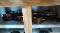 Shelf view showing copper-colored pots and pans with black handles and lids with black knobs.