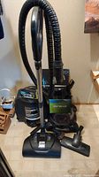 Full view of the upright Purello Ritello vacuum with hose and wand, floor head attached and additional attachment on floor.