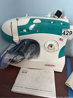Front view of Singer 6038 sewing machine with spool of black thread on top, plastic bag with accessories below, and instruction manual placed next to machine.