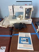 Front full view of JCPenney sewing machine model 4102FE with power cord and manual on table, showing stitch selector dial and accessories tray.