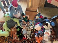 Overview of Wizard of Oz dolls, placemat, and assorted stuffed animals including a green frog, blue Eeyore, brown dog, small leprechaun doll