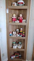Full view of collection on wooden shelving including dolls, ornaments, tins and kitchenware items