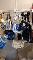 Photo of six women's purses hanging on a rack showing various designs and styles.