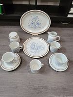 View showing entire set arranged on floor: cups, saucers, sugar bowl with lid, creamer, serving platter, and dinner plate visible with floral blue and gold design