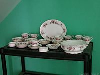 Shuttle rack with multiple cups, saucers, plates and other pieces laid out showing floral patterns of Lavender Rose design and 'Happy Valentine' cups.
