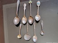 Photo of eight sterling silver collectible spoons laid flat showing varied sizes and decorative handles.