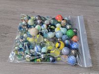 Plastic zip-lock bag filled with assorted vintage marbles of multiple colors and designs against wooden floor background.