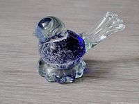 Side view of blue and clear glass bird figurine showing details of the body, head, and tail with textured base.