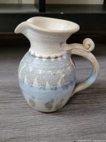 Front angled view of handcrafted jug showing flared spout and curled handle with decorative blue-gray glaze and cream speckled body.