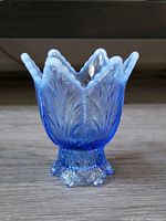 Front angle view of blue opalescent glass vase with ruffled tulip-shaped rim and leaf pattern.