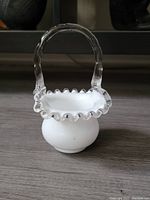 Front angle view of the white glass basket with clear ruffled edge and handle on a dark surface.