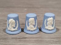 Front view of three Wedgwood blue jasperware thimbles each with a white relief of a king's profile surrounded by a laurel wreath.