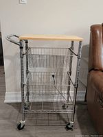Front view of metal kitchen cart showing three wire basket shelves and wooden cutting board top.
