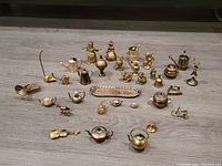 Photo of the full collection arranged on a floor, showing a variety of small brass miniatures including kitchenware, musical instruments, animals, and figurines.