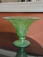 Side view showing the flared, wide top and scale-like textural decoration on the green glass bowl.