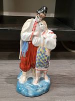 Front view of the painted porcelain figurine showing the couple standing close together on a blue base.
